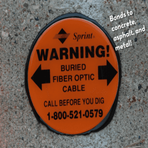 Rhino UV Armor+ Surface Marker Adhesive. Bonds to concrete asphalt, and metal! The marker has a Spring logo and says Warning Buried Fiber Optic Cable Call Before You Dig 1-800-521-0579